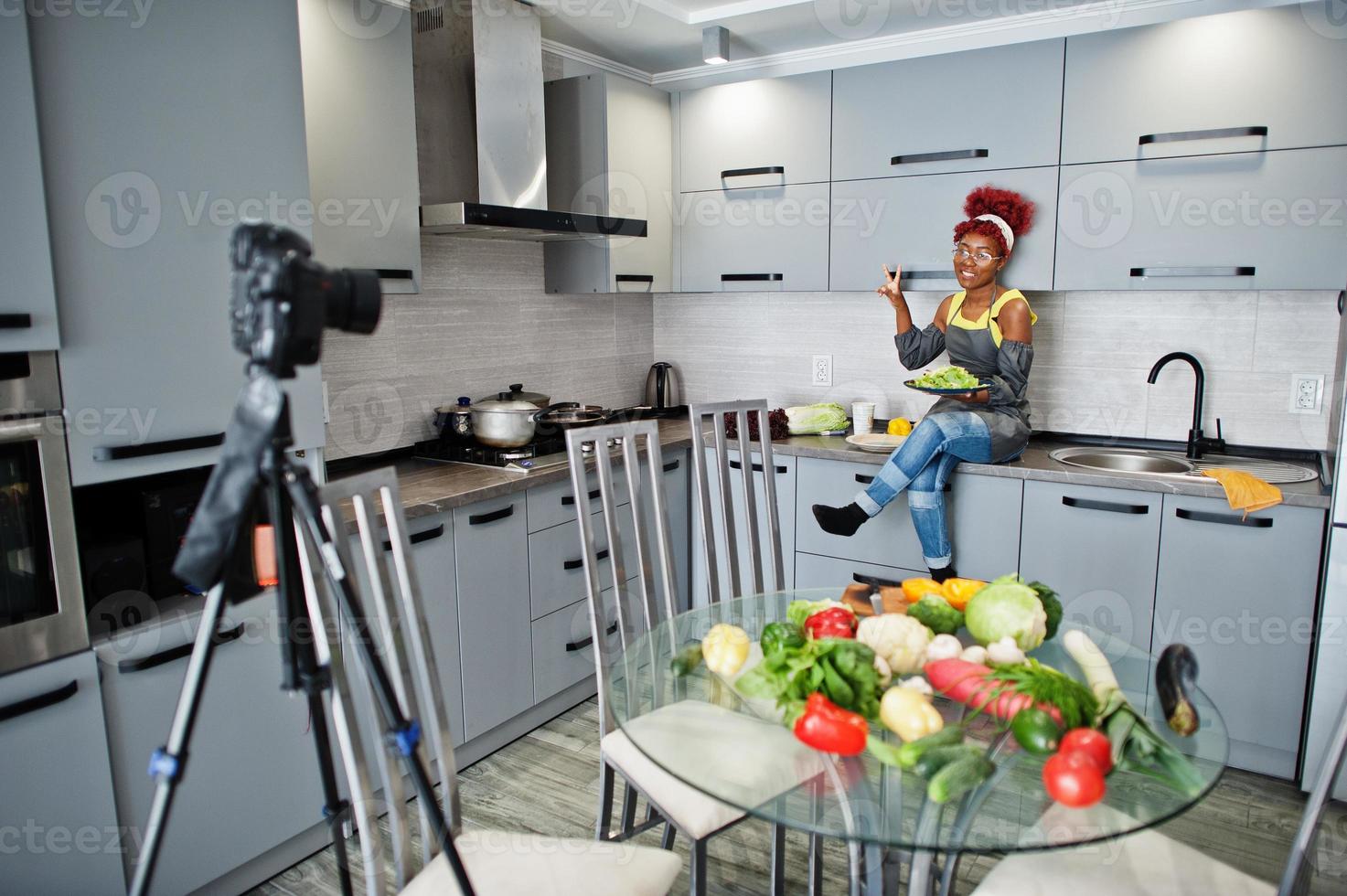 femme afro-américaine filmant son blog diffusé sur des aliments sains dans la cuisine à domicile. elle tient une assiette avec de la salade. photo