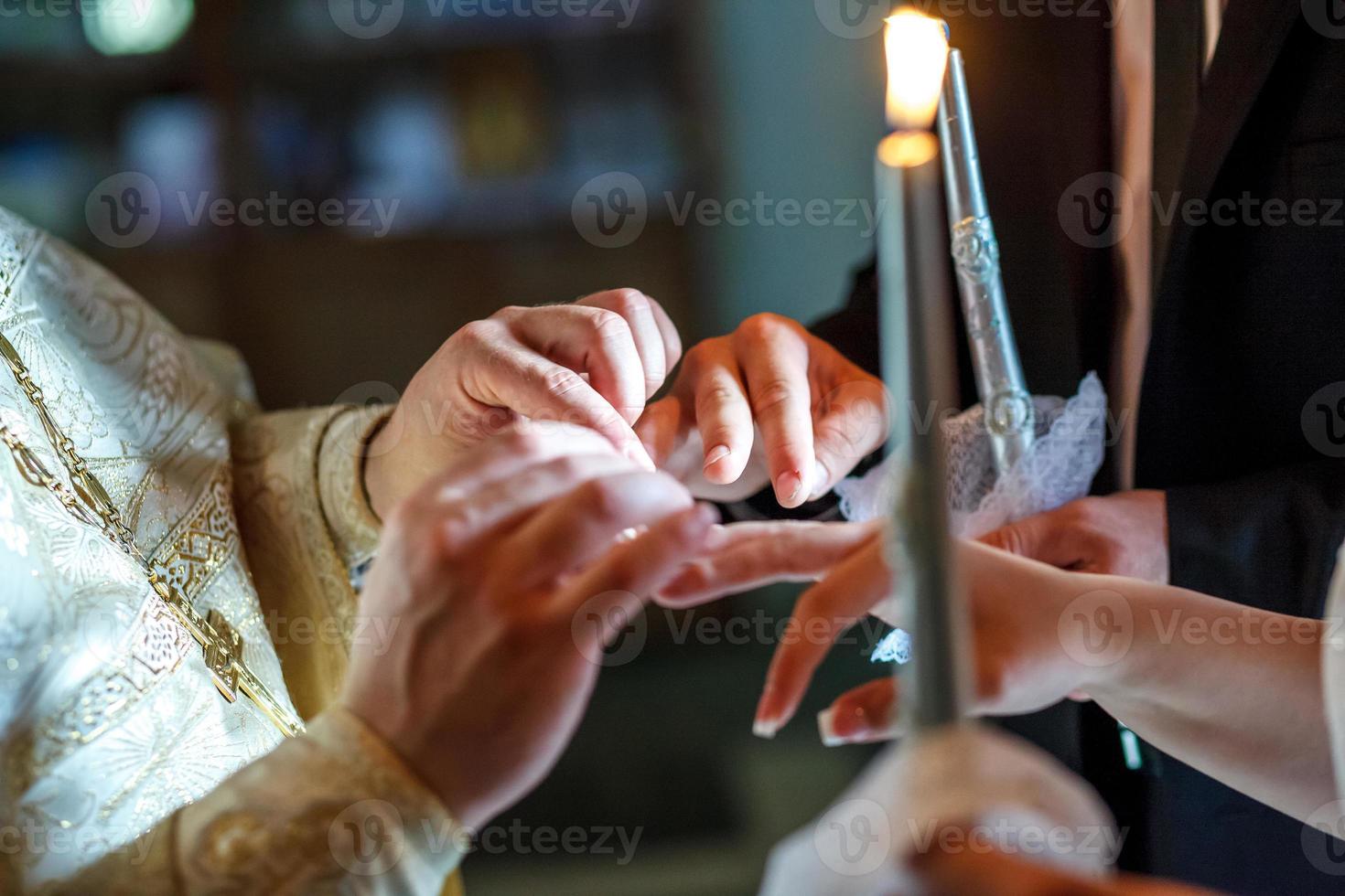 le prêtre aide les jeunes mariés à échanger des alliances lors de la cérémonie de mariage à l'église photo