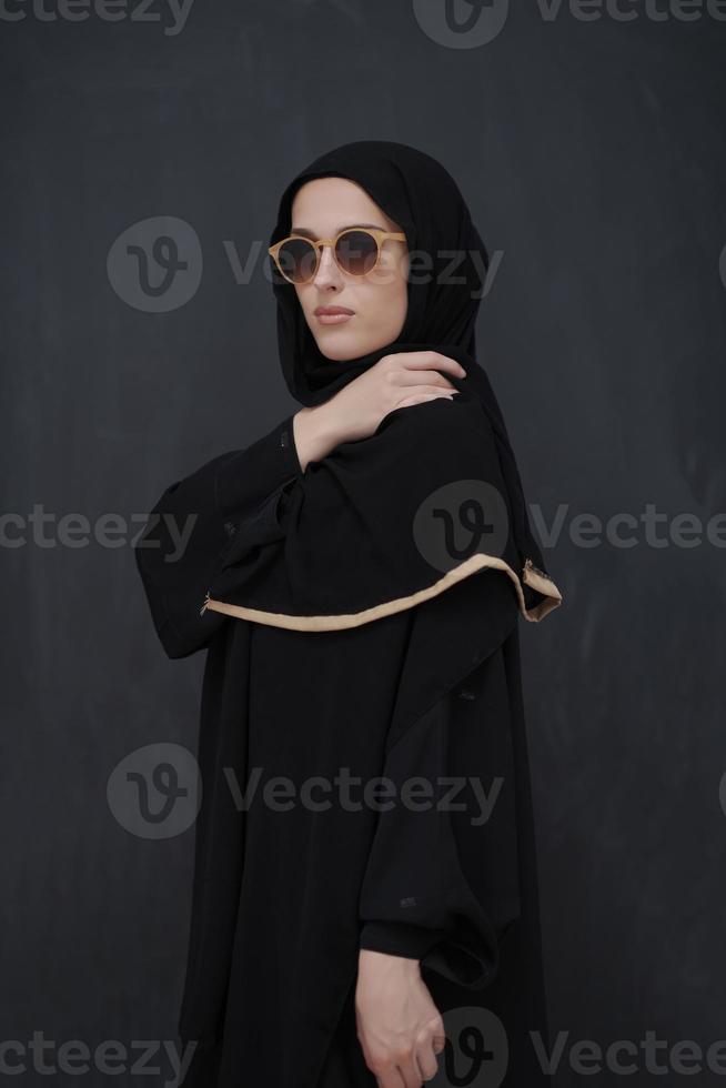 jeune musulman en vêtements traditionnels ou abaya et lunettes de soleil posant devant un tableau noir photo