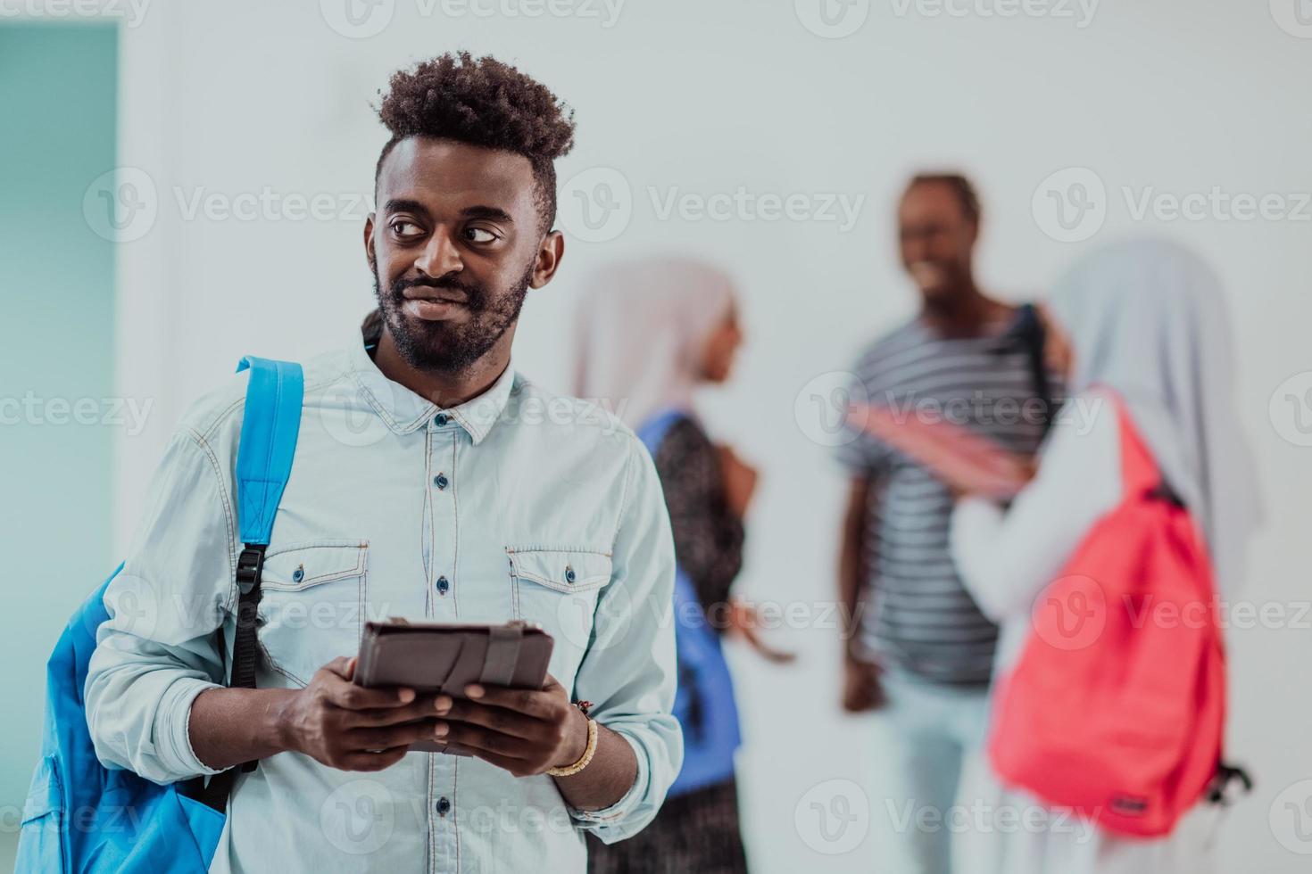 mode de vie universitaire beau jeune étudiant homme tenant une tablette et souriant tout en se tenant contre l'université avec ses amis ont une réunion d'équipe en arrière-plan. photo de haute qualité