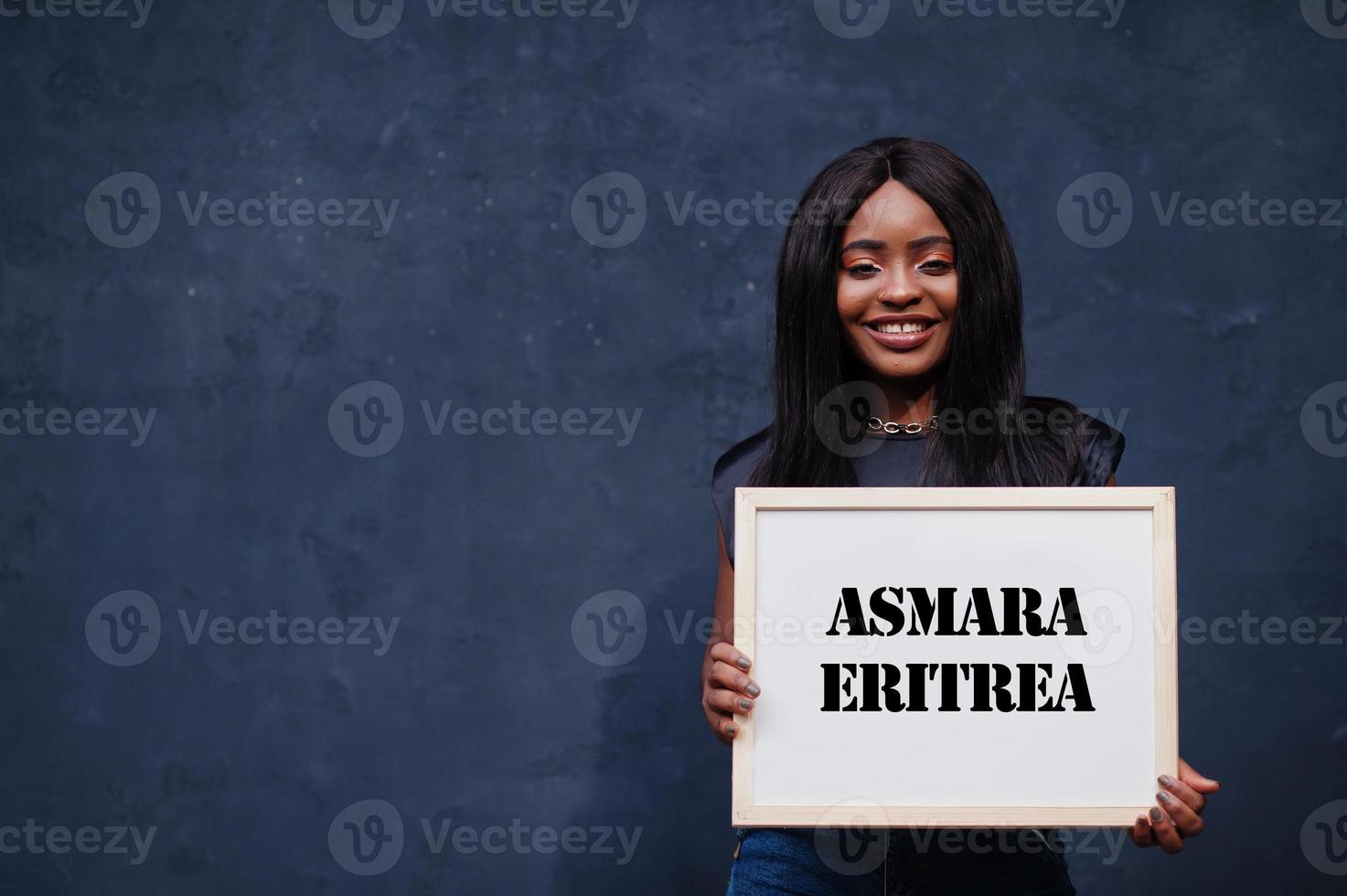 une femme africaine tient un tableau blanc avec l'inscription d'asmara érythrée. concept de ville la plus peuplée d'afrique. photo