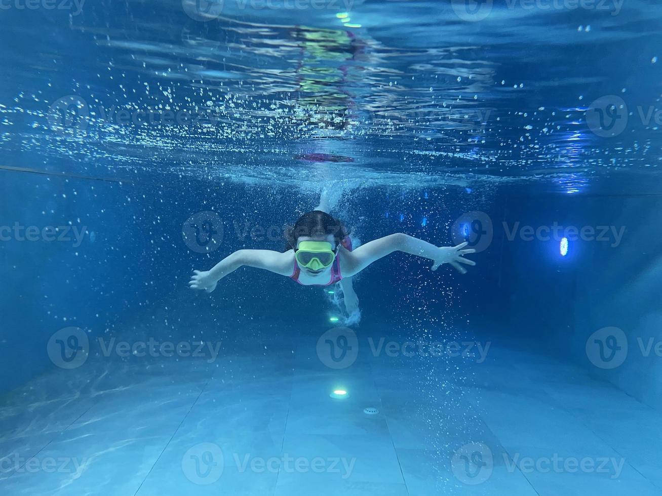 enfant souriant avec des lunettes de natation, plongez dans la piscine avec plaisir - sautez profondément sous l'eau. mode de vie sain, activité de sports nautiques les étés. photo