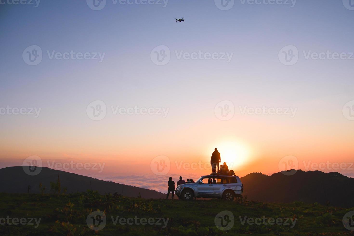 groupe de voyageurs créateurs de contenu se tiennent à côté d'un véhicule 4x4 ensemble à l'extérieur dans l'aventure de la nature regarder le coucher du soleil sur l'horizon sur cloudscape dans la nature. découverte et aventure photo