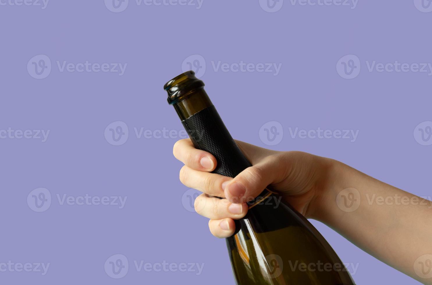 a woman's hand holding an open bottle of champagne on a lilas background.very peri photo