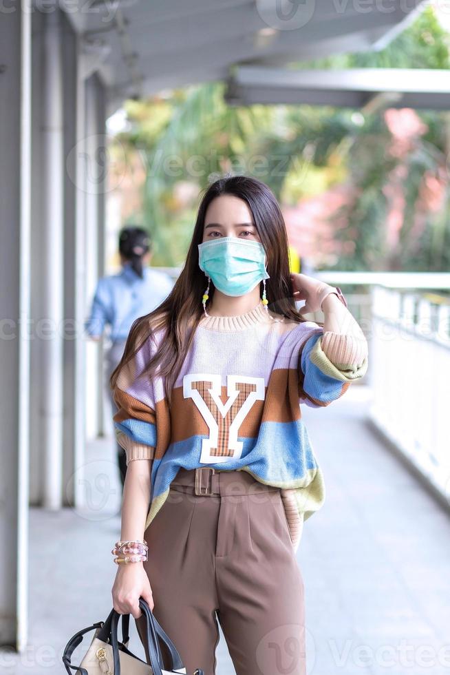 une belle femme asiatique marchant dans la ville porte des chandails colorés, des cheveux longs et des masques médicaux dans un nouveau concept normal de pollution pm2,5 et de soins de santé. photo