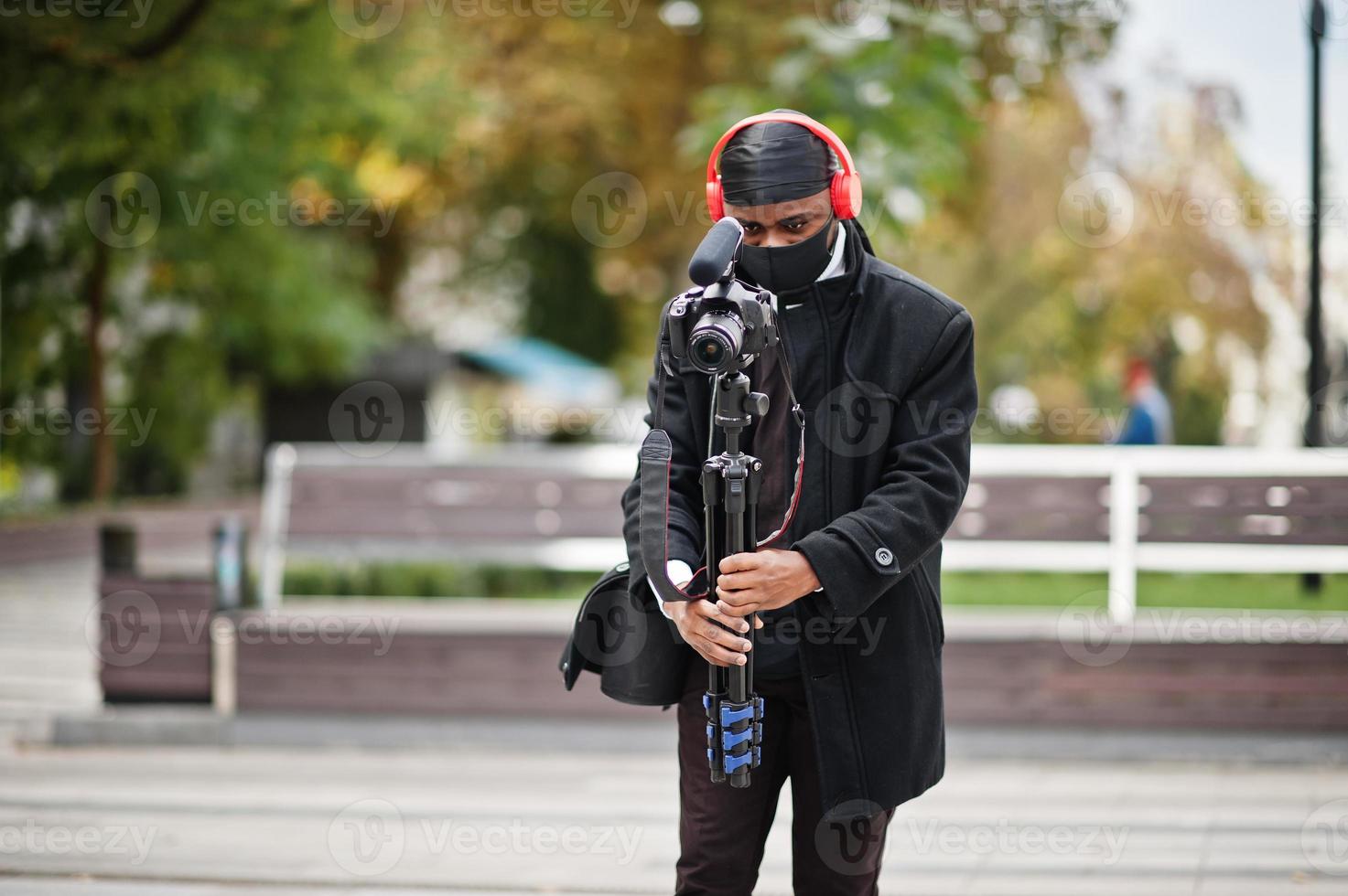 jeune vidéaste afro-américain professionnel tenant une caméra professionnelle avec un équipement professionnel. caméraman afro portant du duraq noir et un masque de protection du visage, faisant des vidéos. photo