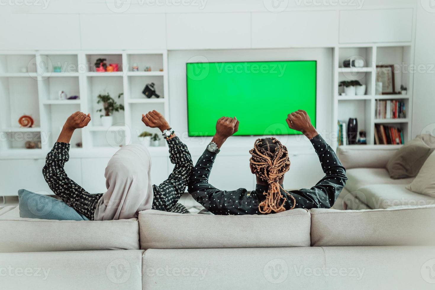 couple africain assis sur un canapé en regardant la télévision ensemble écran vert chroma femme portant des vêtements islamiques en hijab photo