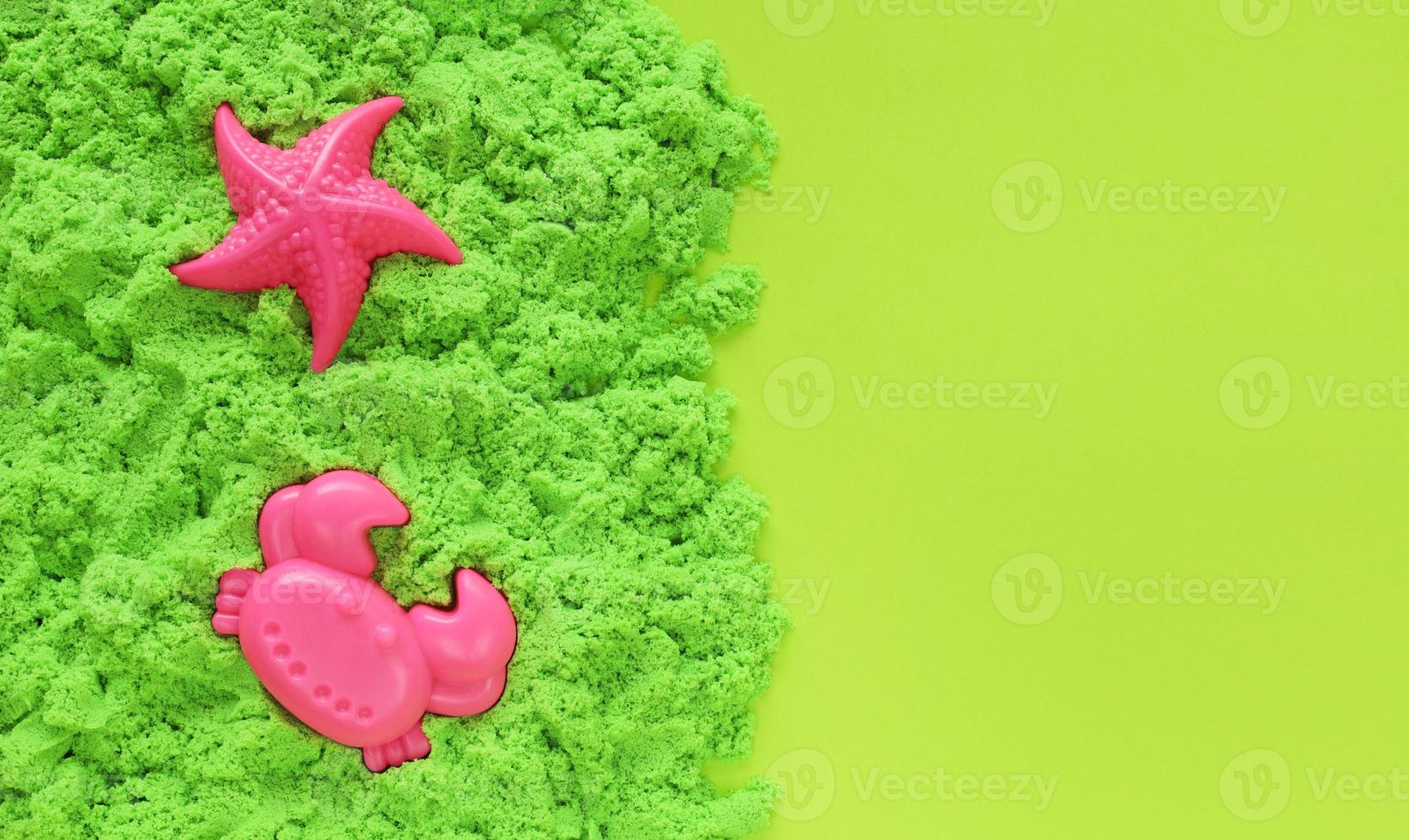 sable cinétique vert avec deux moules à sable en plastique rose en forme d'étoile de mer et de crabe. jeu sensoriel pour enfants. temps libre sur le concept de vacances. fond de papier vert clair avec espace de copie. photo