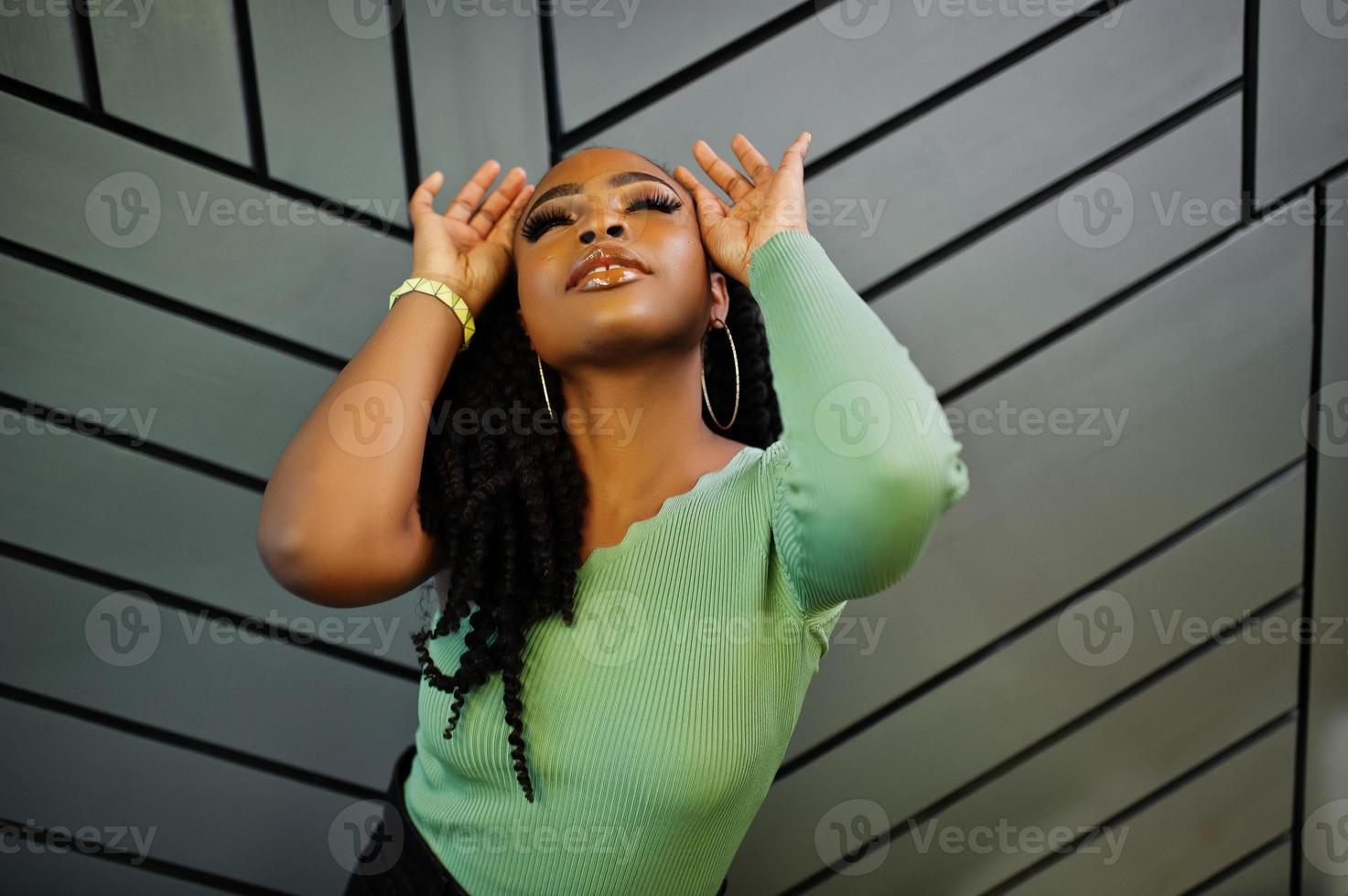 portrait d'une jeune femme afro-américaine séduisante portant un pull vert posant contre un mur gris. photo