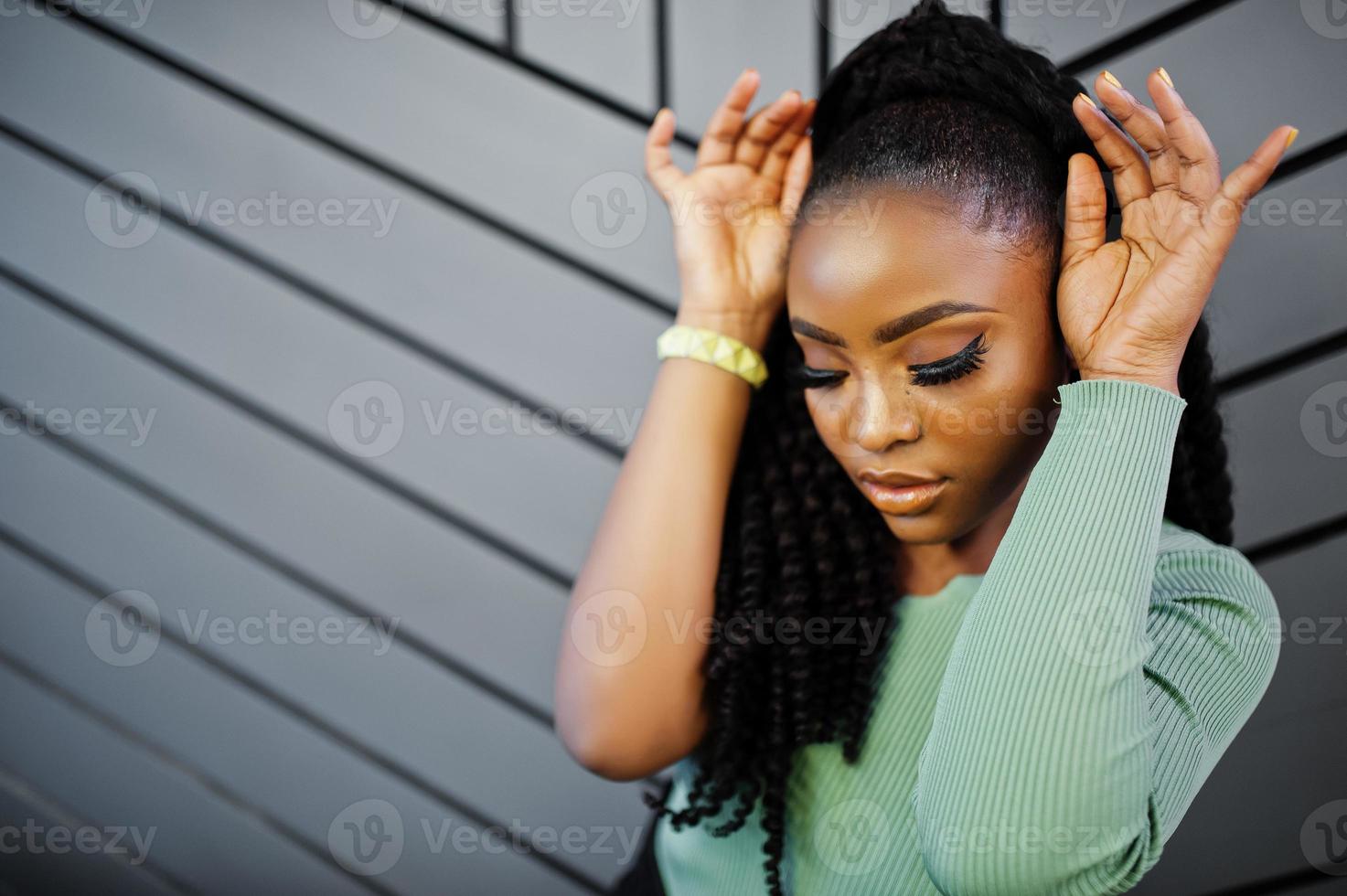 portrait d'une jeune femme afro-américaine séduisante portant un pull vert posant contre un mur gris. photo