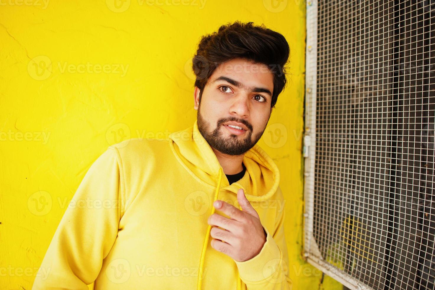 jeune homme indien hipster urbain dans un sweat-shirt jaune à la mode. un gars sud-asiatique cool porte un sweat à capuche. photo