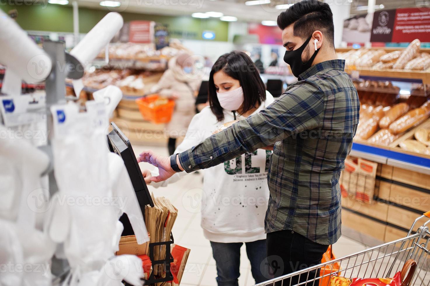 un couple asiatique porte un masque protecteur faisant ses courses ensemble dans un supermarché pendant la pandémie. prenez un autocollant du moniteur pour les produits de boulangerie de pain. photo