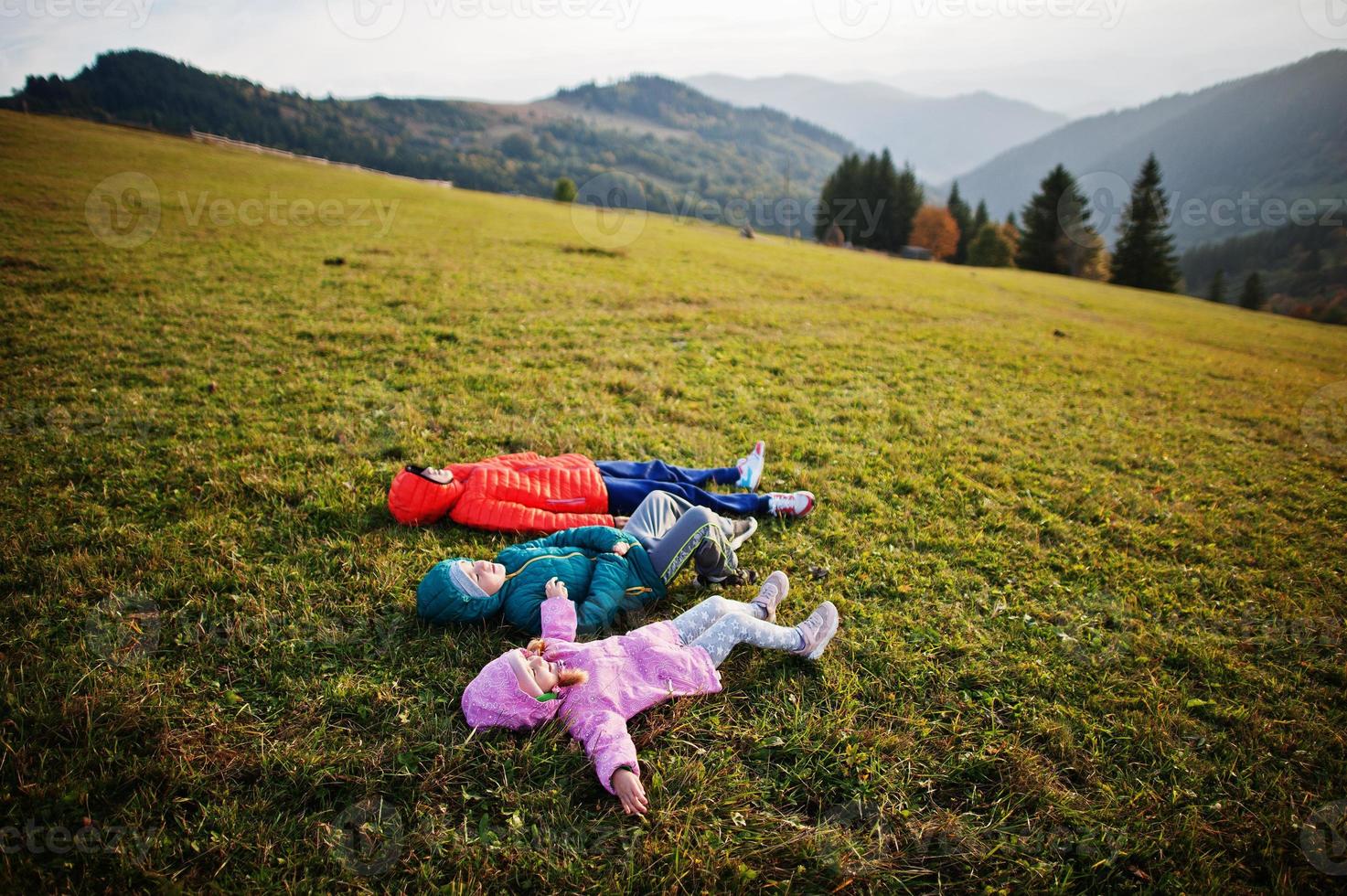 trois enfants allongés dans l'herbe avec une magnifique chaîne de montagnes à l'horizon. photo