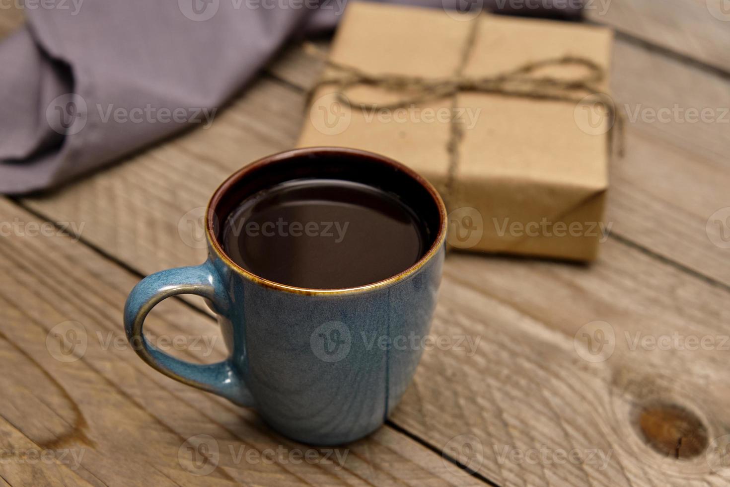 tasse de café noir sur une table en bois à côté du cadeau enveloppé dans du papier kraft photo