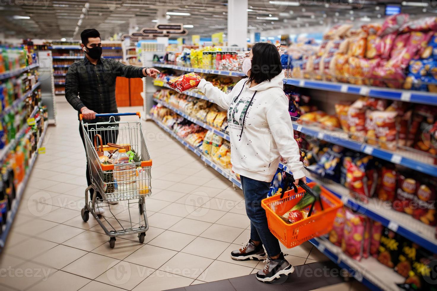 un couple asiatique porte un masque protecteur faisant ses courses ensemble dans un supermarché pendant la pandémie. prendre des collations différentes. photo