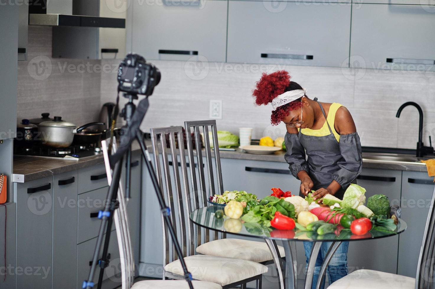 femme afro-américaine filmant son blog diffusé sur des aliments sains dans la cuisine à domicile. elle coupe le chou. photo