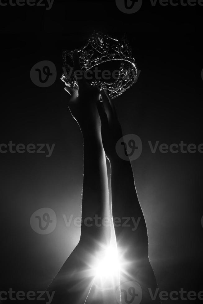 la silhouette abstraite de deux mains essaie d'atteindre la couronne de diamants en tant que concours de concours de reine de beauté Miss en tant que compétition finale, moment du vainqueur final. fumée rétroéclairée faible exposition fond sombre espace de copie photo