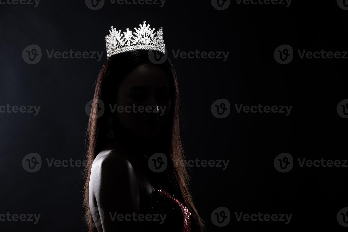 portrait du concours de beauté de miss pageant en robe de soirée à sequins robe longue avec couronne de diamants scintillants, silhouette exposition discrète avec rideau, éclairage de studio fond sombre dramatique photo
