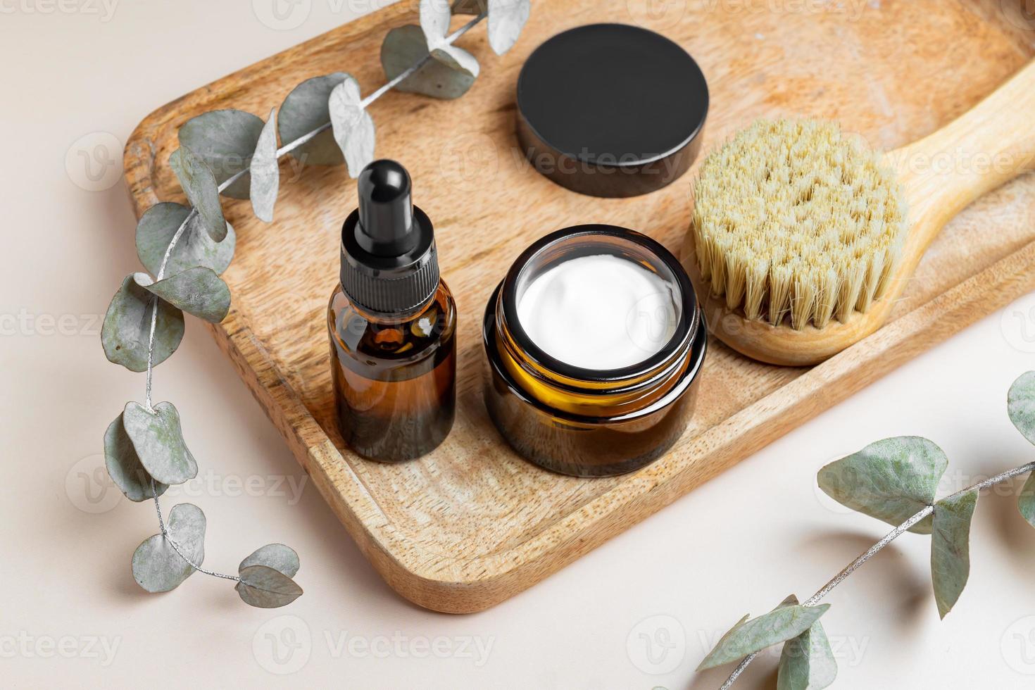 concept d'exfoliation et de rajeunissement de la peau. flacon compte-gouttes avec peeling aux fruits, masque facial et brosse de massage pour le visage avec poils naturels sur plateau en bois avec feuilles d'eucalyptus. photo