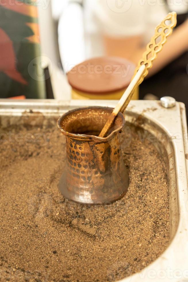 café turc préparé sur du sable chaud pour un goût et un arôme uniques. boisson orientale traditionnelle en cezve de cuivre photo