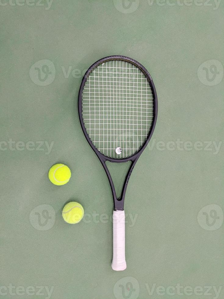 vue de dessus de la raquette de tennis et de deux balles sur le court de tennis en terre battue verte photo