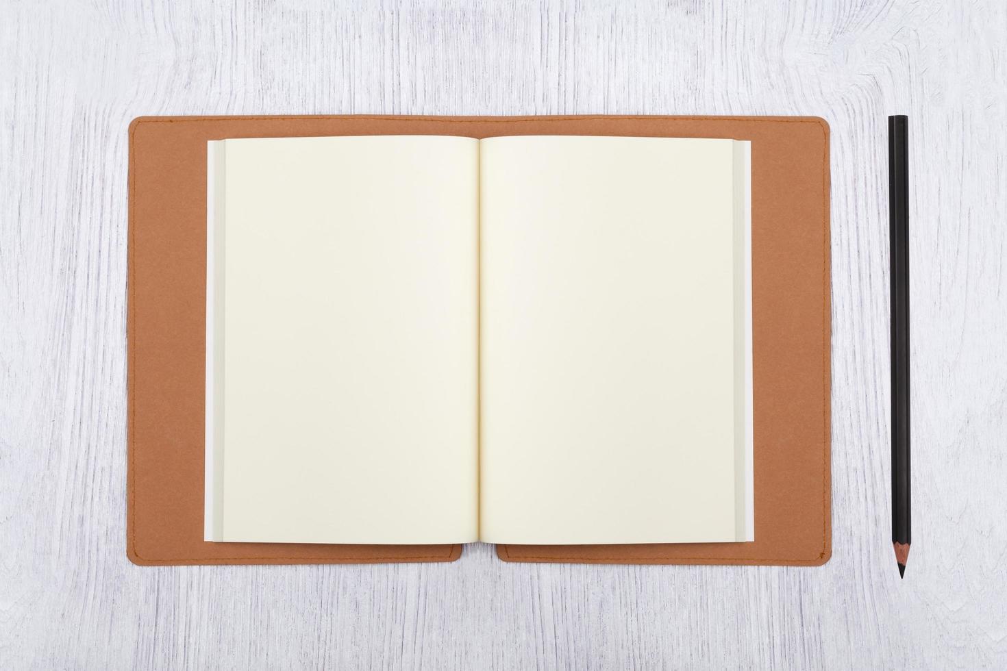 cahier marron ouvert et un crayon sur une table en bois blanc, vue de dessus photo