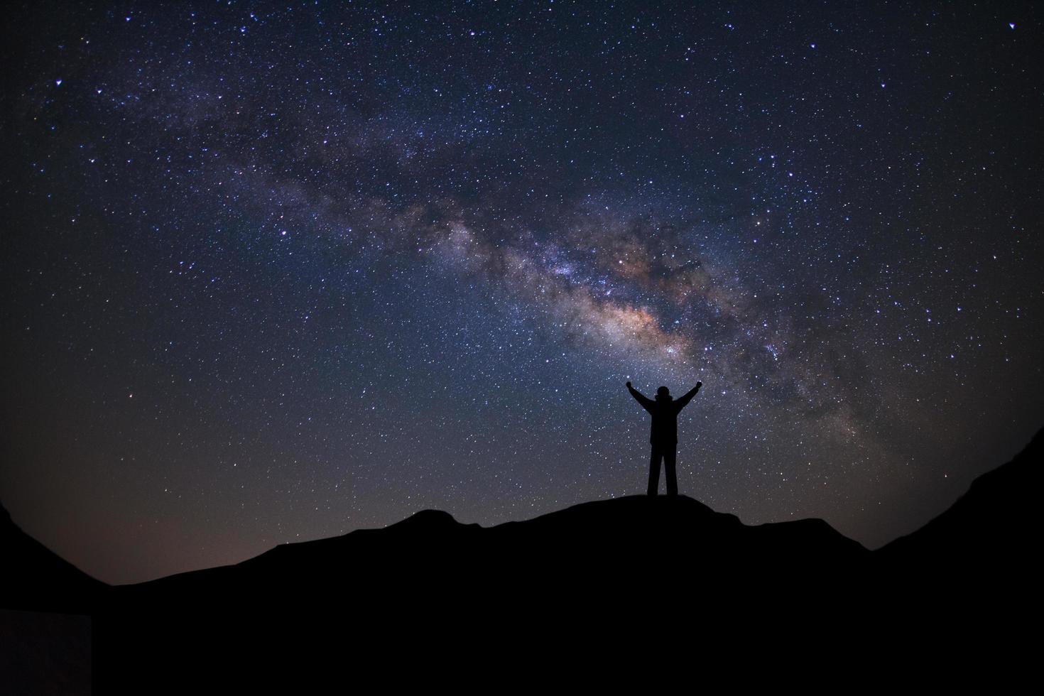 paysage panoramique avec voie lactée, ciel nocturne avec étoiles et silhouette d'un homme sportif debout avec les bras levés sur la haute montagne. photo