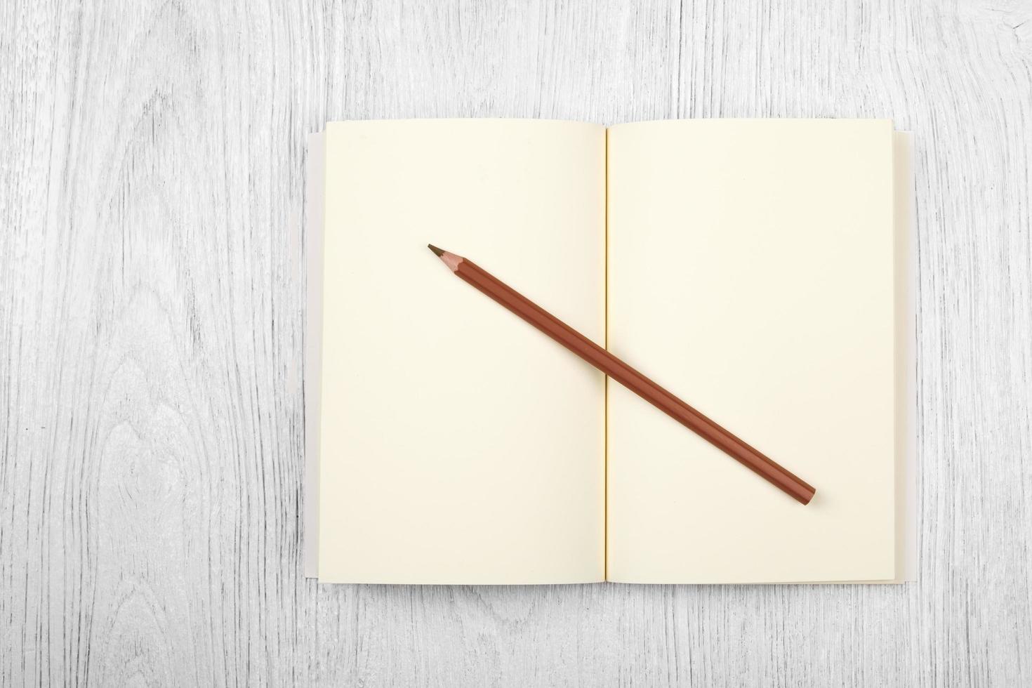 cahier marron ouvert et un crayon sur une table en bois blanc, vue de dessus photo