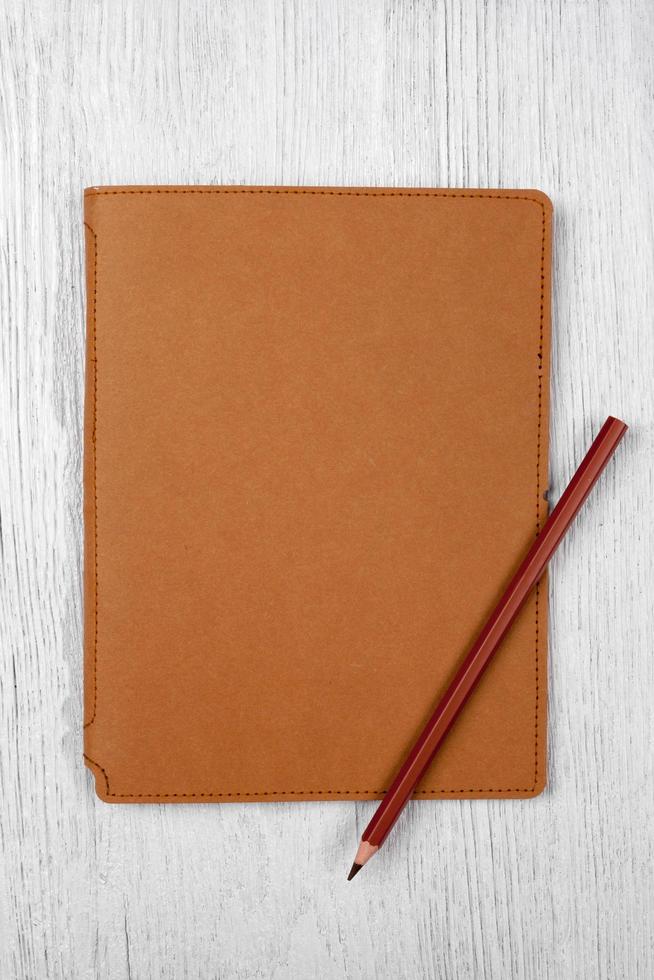 cahier marron et un crayon sur une table en bois blanc, vue de dessus photo