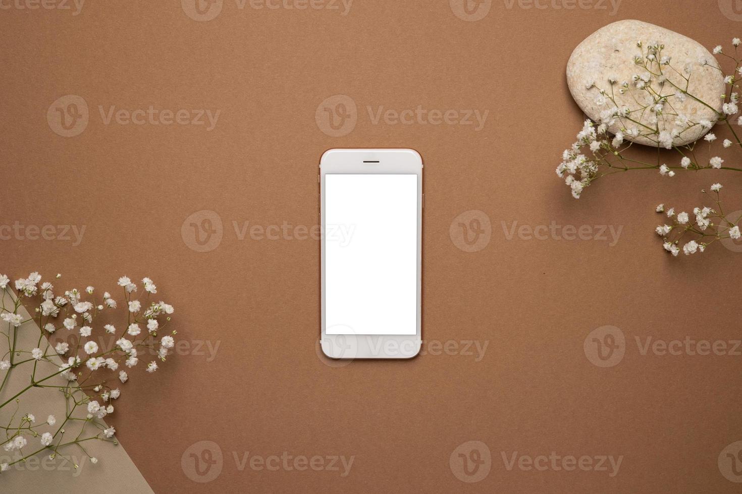 téléphone portable avec écran blanc et branche de fleurs sèches et pierre sur fond marron clair. tendance, concept minimal avec fond photo