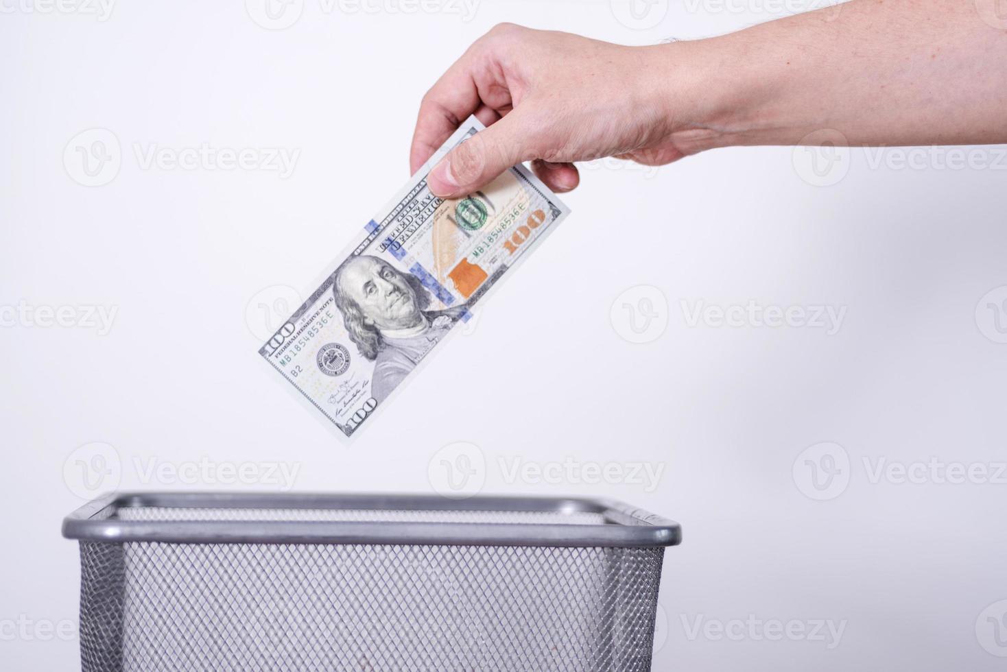 une main jette des billets d'un dollar dans une poubelle sur fond gris. photo