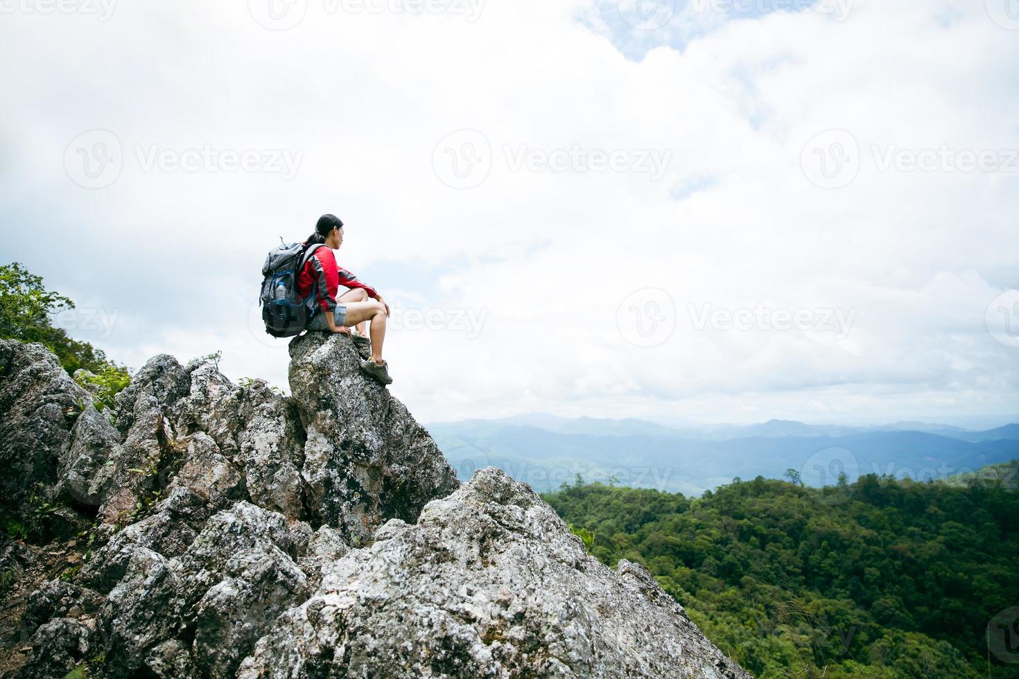 jeune personne randonnée femme assise sur le dessus du rocher, sac à dos femme regardant la belle vallée de montagne à la lumière du soleil en été, paysage avec fille sportive, hautes collines, forêt, ciel. voyage et tourisme. photo