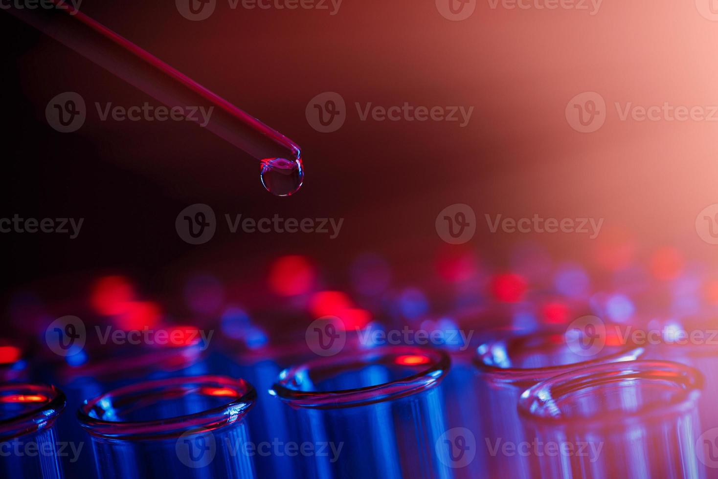 rangée de tubes à essai. concept de laboratoire médical ou scientifique, gouttelette liquide avec compte-gouttes sur fond bleu rouge, gros plan, photo macro.