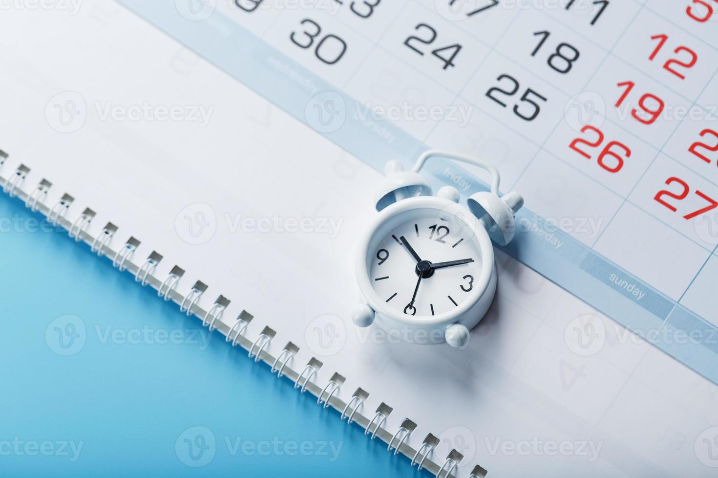 l'heure sur un réveil blanc allongé sur le calendrier et un fond bleu. photo