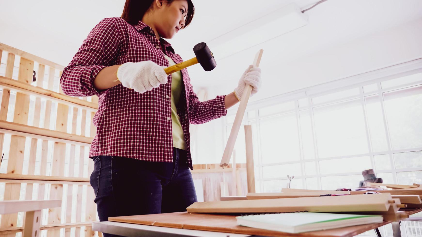 charpentier féminin utilisant un marteau pour enfoncer des clous dans la planche sur le site. photo