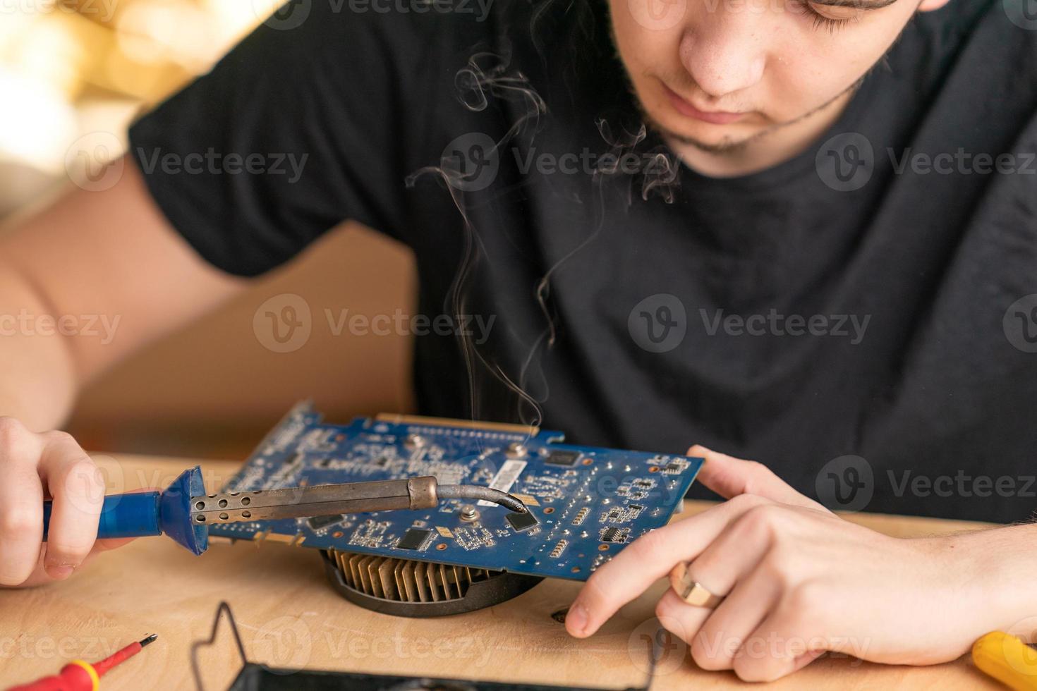 un jeune homme soude un microcircuit brûlé avec un fer à souder photo