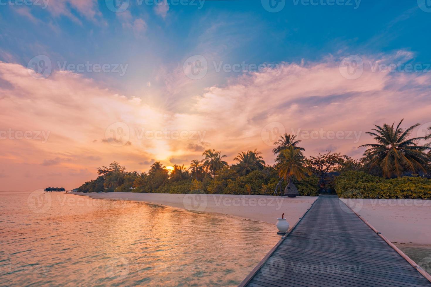 coucher de soleil sur l'île des maldives, voie de la jetée en bois du complexe de luxe. fantastique ciel coloré nuages reflet plage mer horizon. vacances d'été romantiques, concept de voyage. paysage de coucher de soleil paradisiaque photo