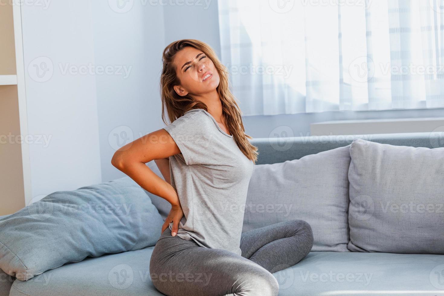 femme souffrant de maux de dos à la maison. douleur dans le bas du dos . une femme ressent des maux de dos en massant des muscles endoloris, une femme triste souffre de lombalgie photo