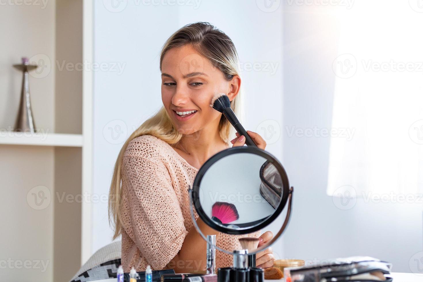 beauté femme se maquiller. belle fille regardant dans le miroir et appliquant un cosmétique avec un gros pinceau. la fille rougit sur les pommettes. poudre, rouge photo