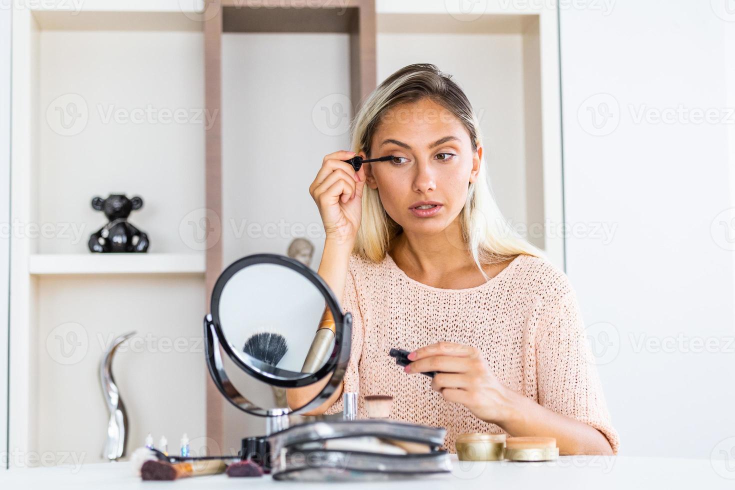 belle femme appliquant du maquillage peindre ses cils pour un rendez-vous en soirée devant un miroir. photo