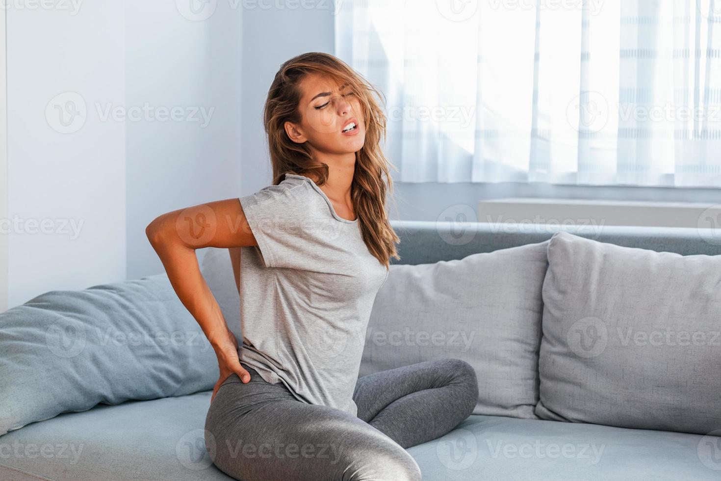 femme souffrant de maux de dos à la maison. douleur dans le bas du dos . une femme ressent des maux de dos en massant des muscles endoloris, une femme triste souffre de lombalgie photo