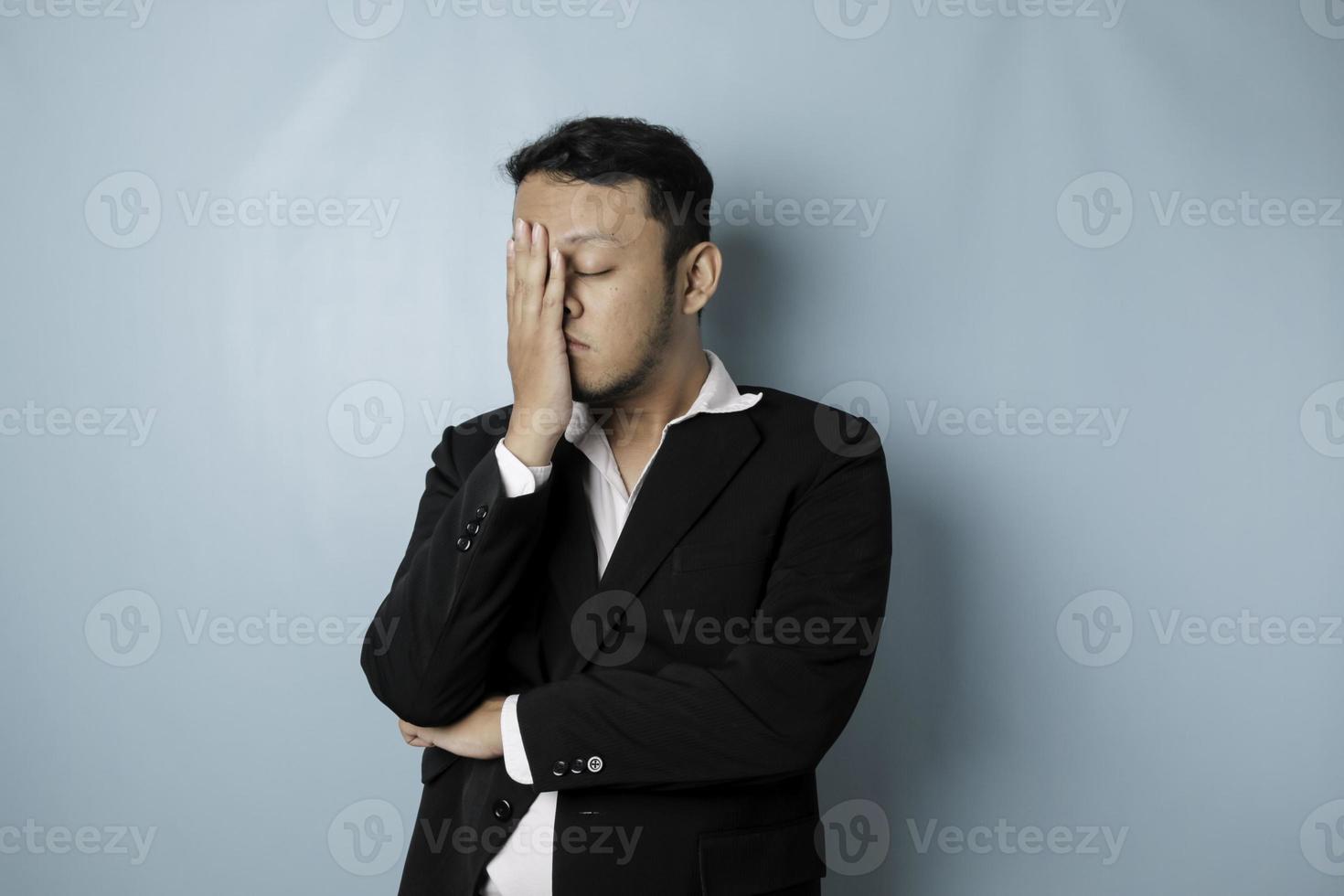 l'homme d'affaires asiatique a l'air fatigué et déprimé, a une expression triste tout en se tenant la tête. fond bleu isolé photo