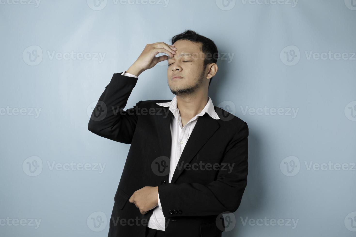 l'homme d'affaires asiatique a l'air fatigué et déprimé, a une expression triste tout en se tenant la tête. fond bleu isolé photo