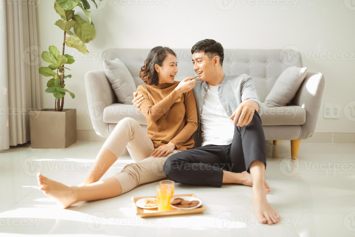 détente à la maison. heureux jeune homme et femme buvant une boisson chaude avec une pâte sucrée. ils sont assis à table sur le sol près du canapé et sourient photo