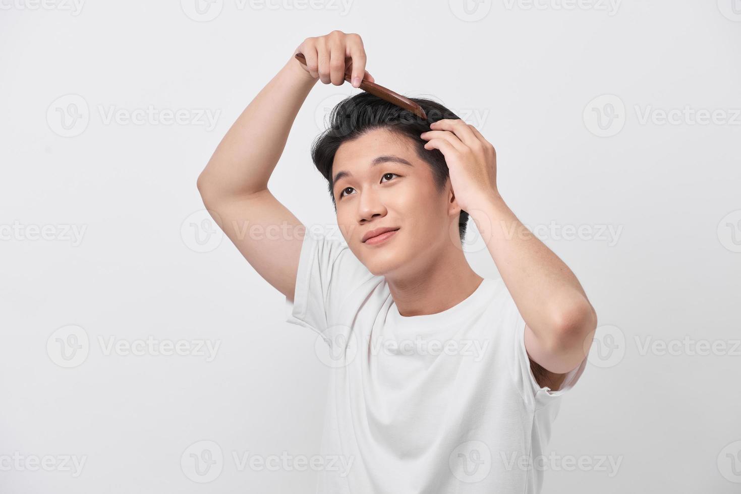 concept de beauté, de toilettage et de personnes - jeune homme souriant se brosser les cheveux avec un peigne sur fond blanc photo