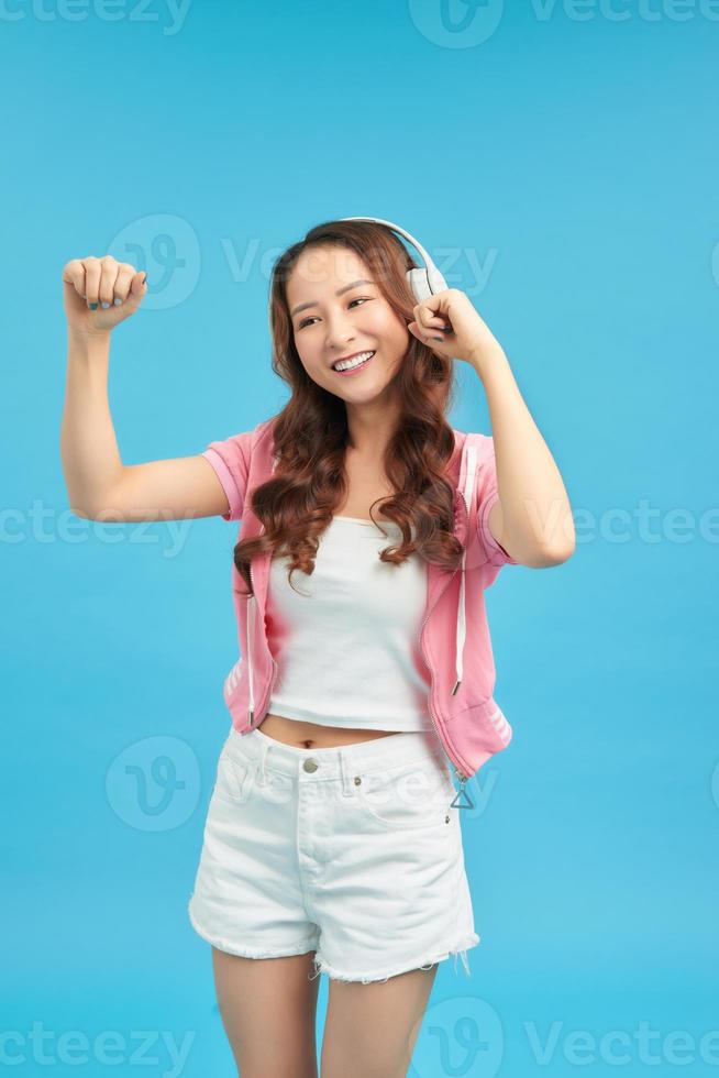 portrait d'une fille souriante et satisfaite habillée en écoutant de la musique avec des écouteurs en se tenant debout sur fond bleu photo