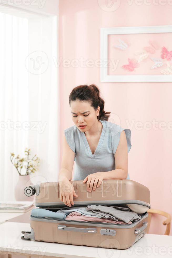 femme prépare une valise de voyage à la maison. femme excitée essayant de fermer une valise pleine. photo