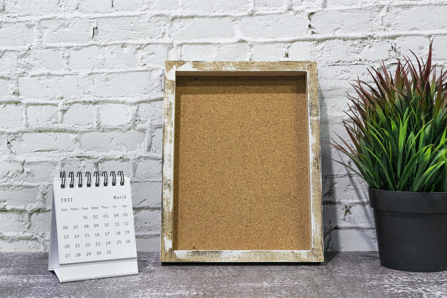 calendrier blanc de mars 2022 avec cadre en bois et plante en pot sur un bureau en bois. photo