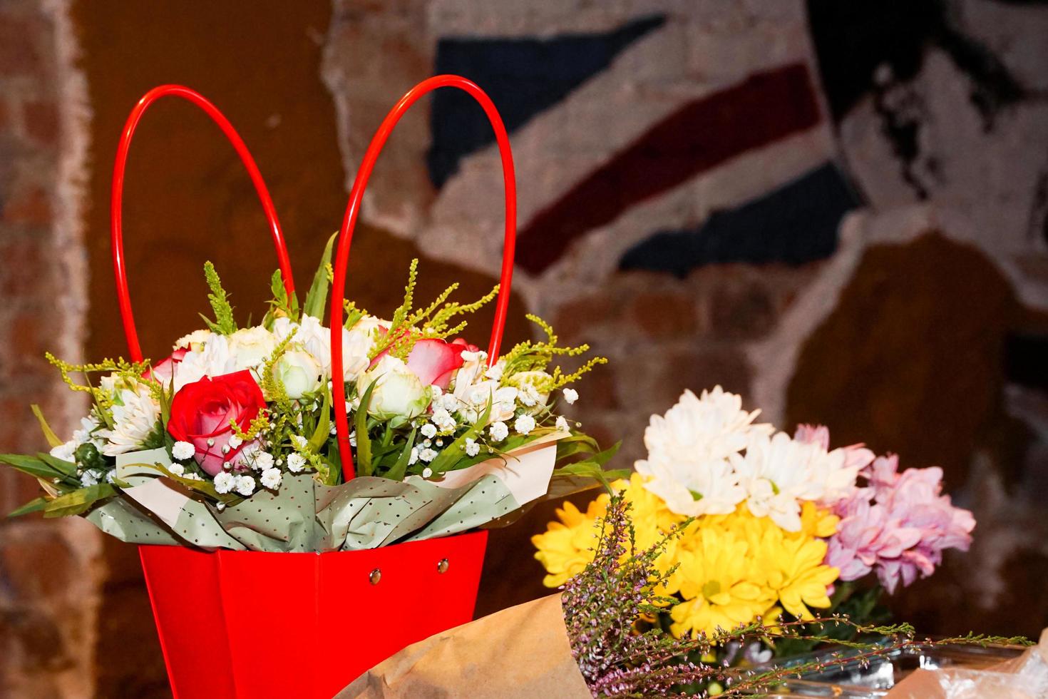 bouquet de fleurs dans un panier rouge et en papier kraft contre un mur de briques floues photo