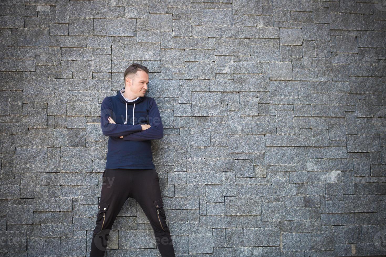 homme aux bras croisés appuyé sur un mur de briques. photo